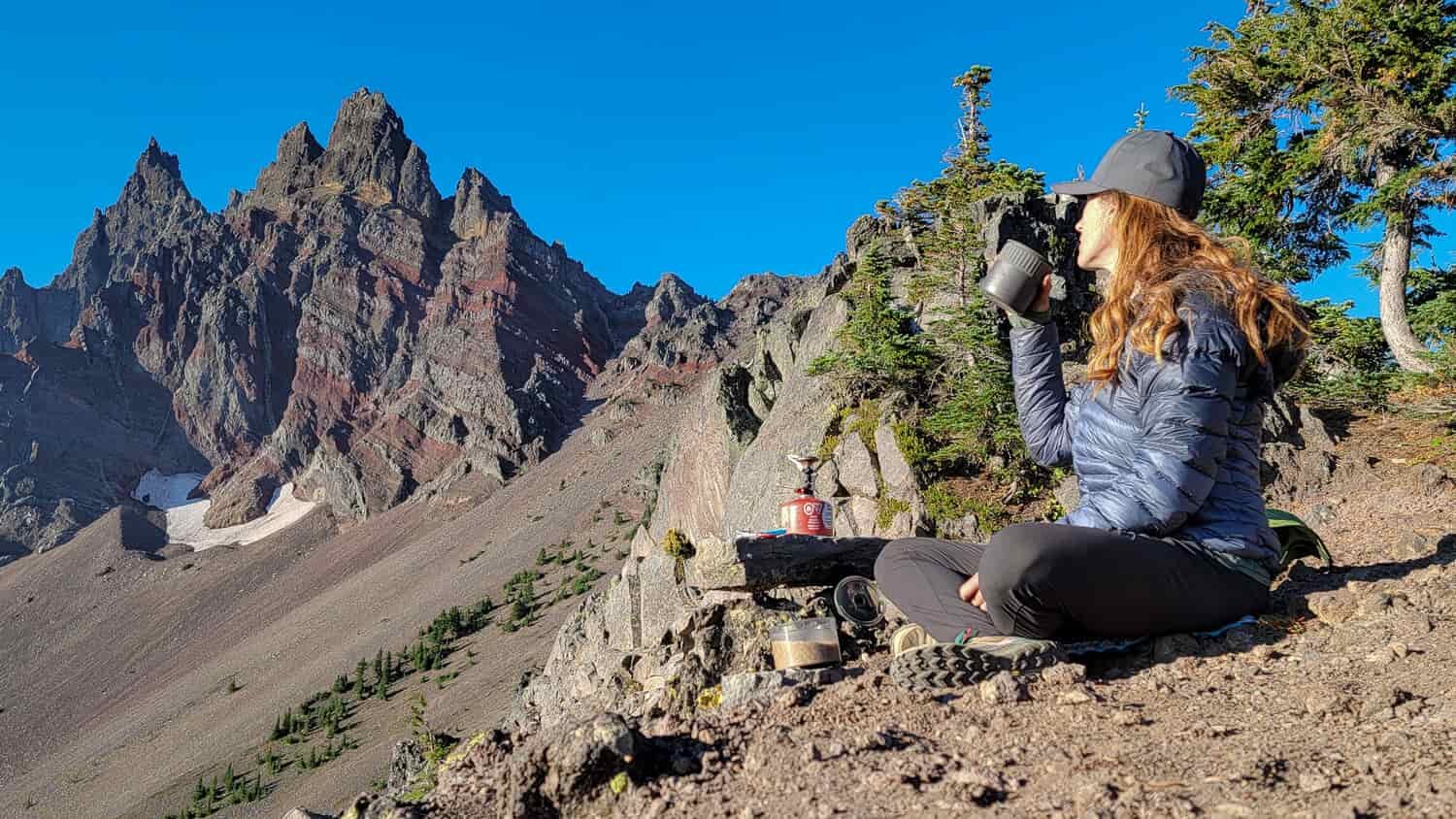 a backpacker drinking coffee with a view of the craggy ridge of three finger jack