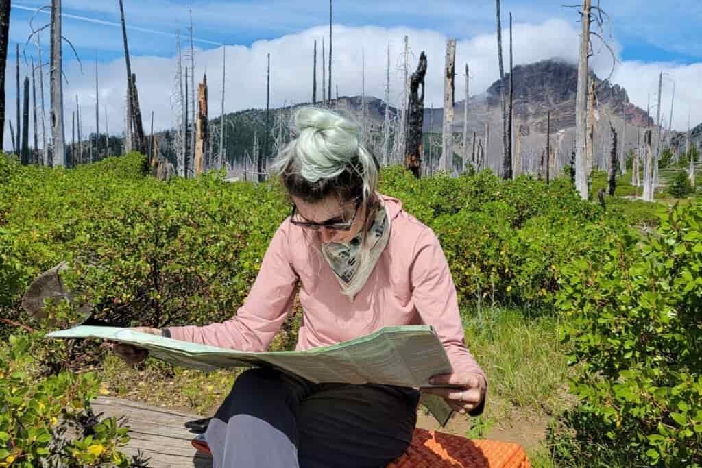backpacker sitting on a log reading their map in with three fingered jack in the background 