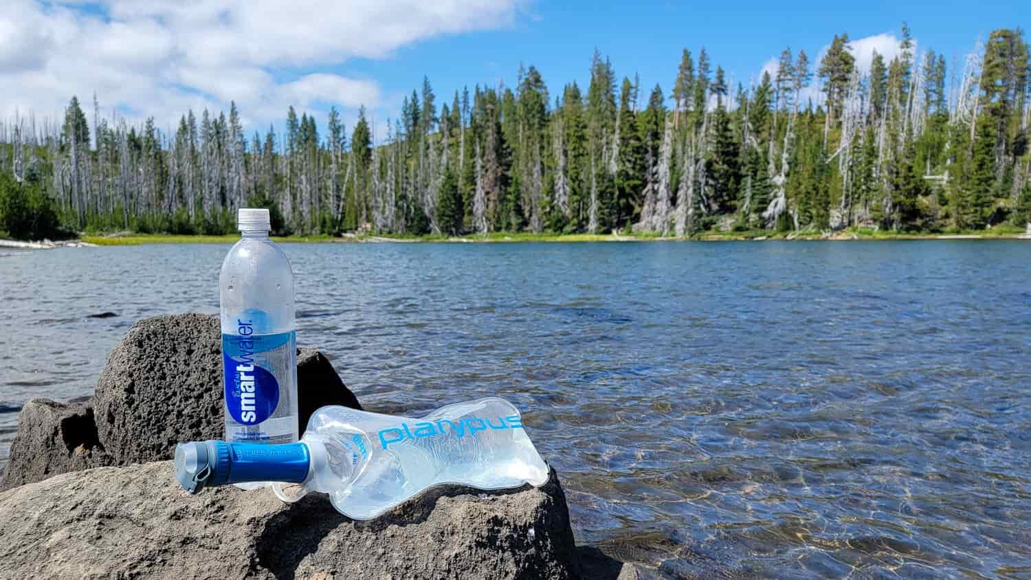 A lake with a backpacker's water filter system refilling their bottles and bladders