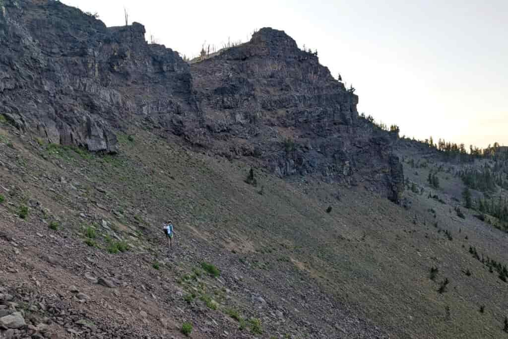 backpacker below a craggy cirque traversing a scree field on a narrow trail