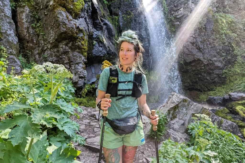 backpacker holding trekking poles next to a small waterfall in the blue mountains