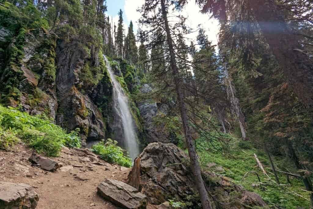 waterfall called strawberry falls with green plants and larches and douglas firs around it