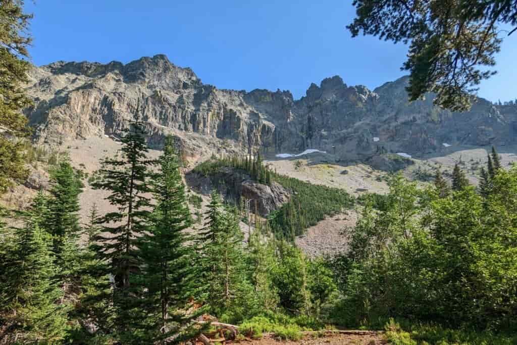 cliffs and craggy spires with scree fields below and conifers in the foreground surround little strawberry lake