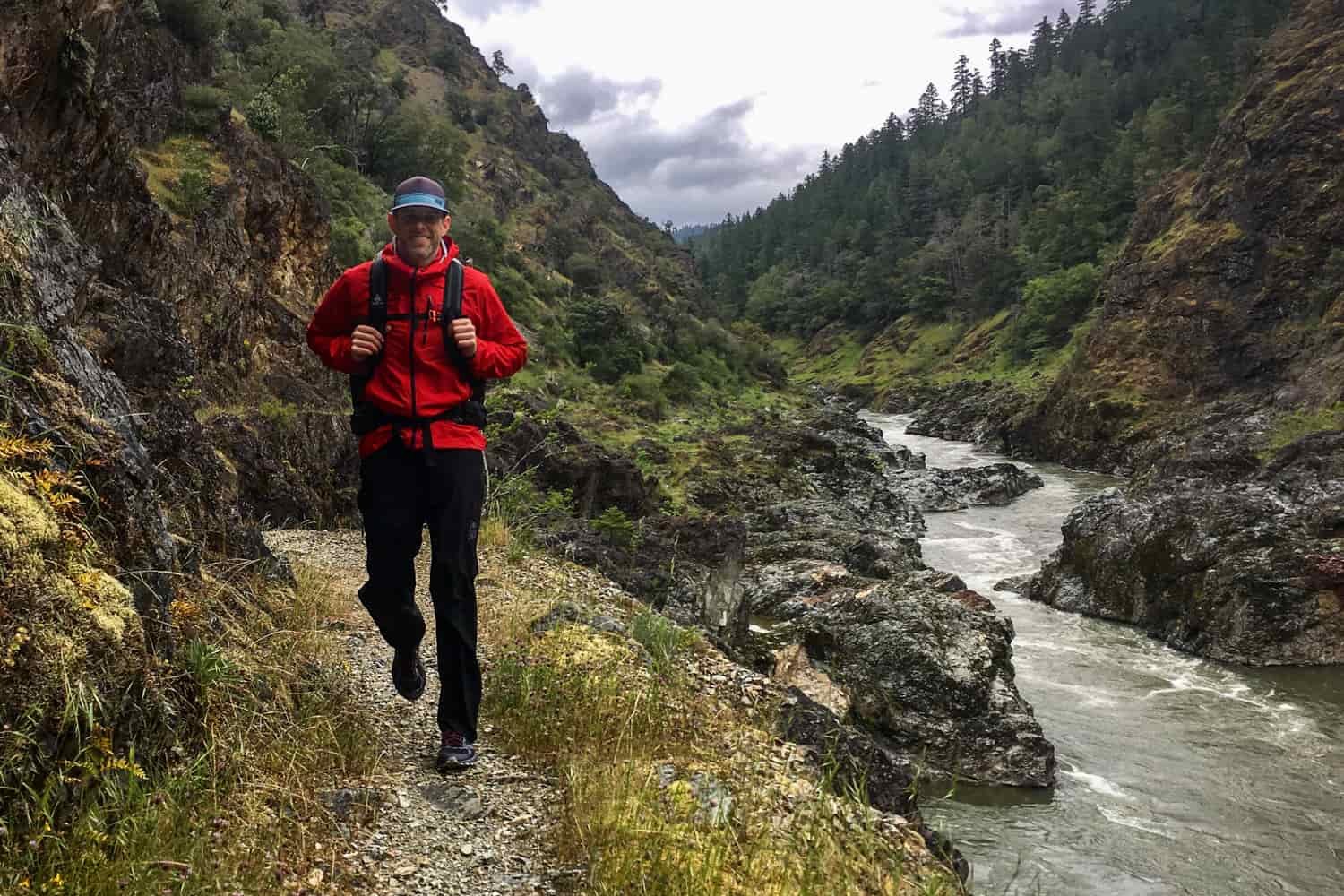 backpacker on the rogue river trail with the rushing water to their left and cliffs towering above them on the right.