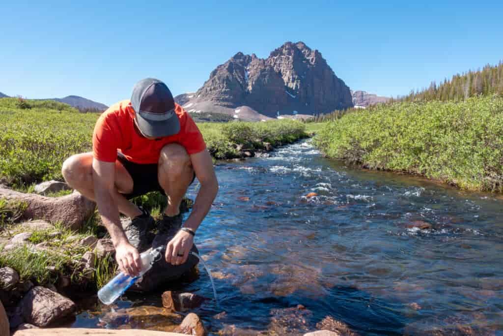 The author filters water from a small mountain stream which ripples down from a distant mountain