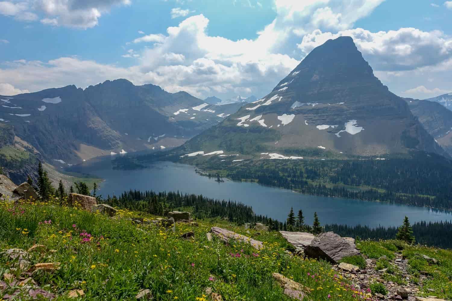 big lake curving around a pyramid shaped peak in glacier national park.