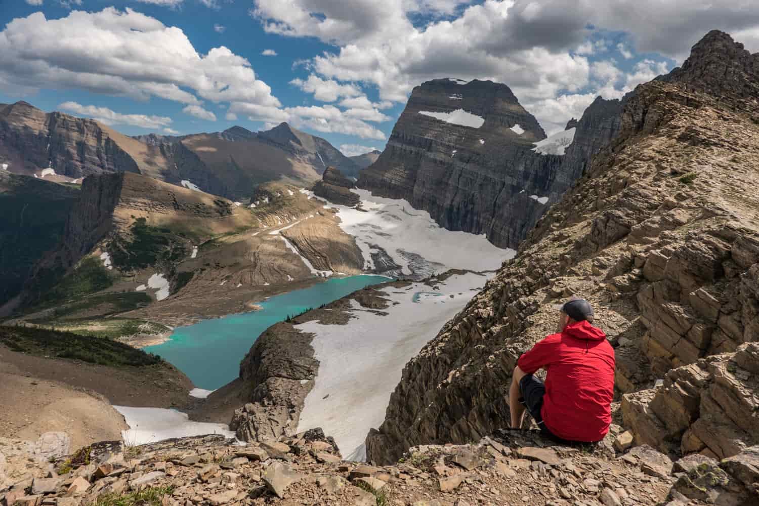 hiker seated above a glacier and its tarn in glacier national park