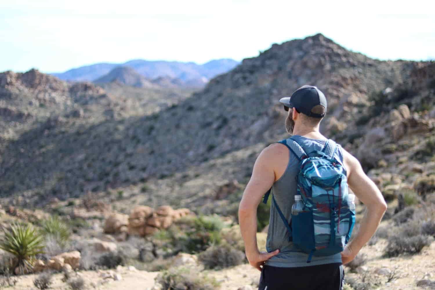 A male hiker in a daypack peers over a wash in Joshua Tree National Park