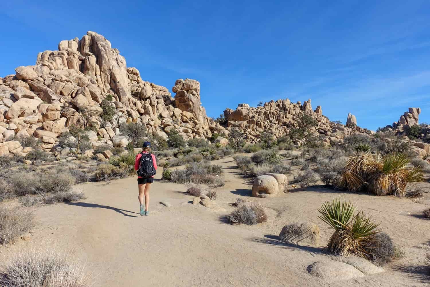 A woman walks up a sandy wash toward stacked rock formations
