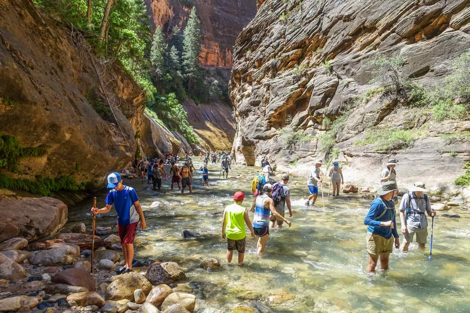 lots of people walking through the water in the temple of sinawava in zion national park