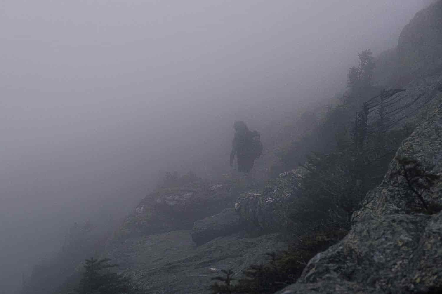 backpacker on the long trail walking on a rocky slope in dense fog.