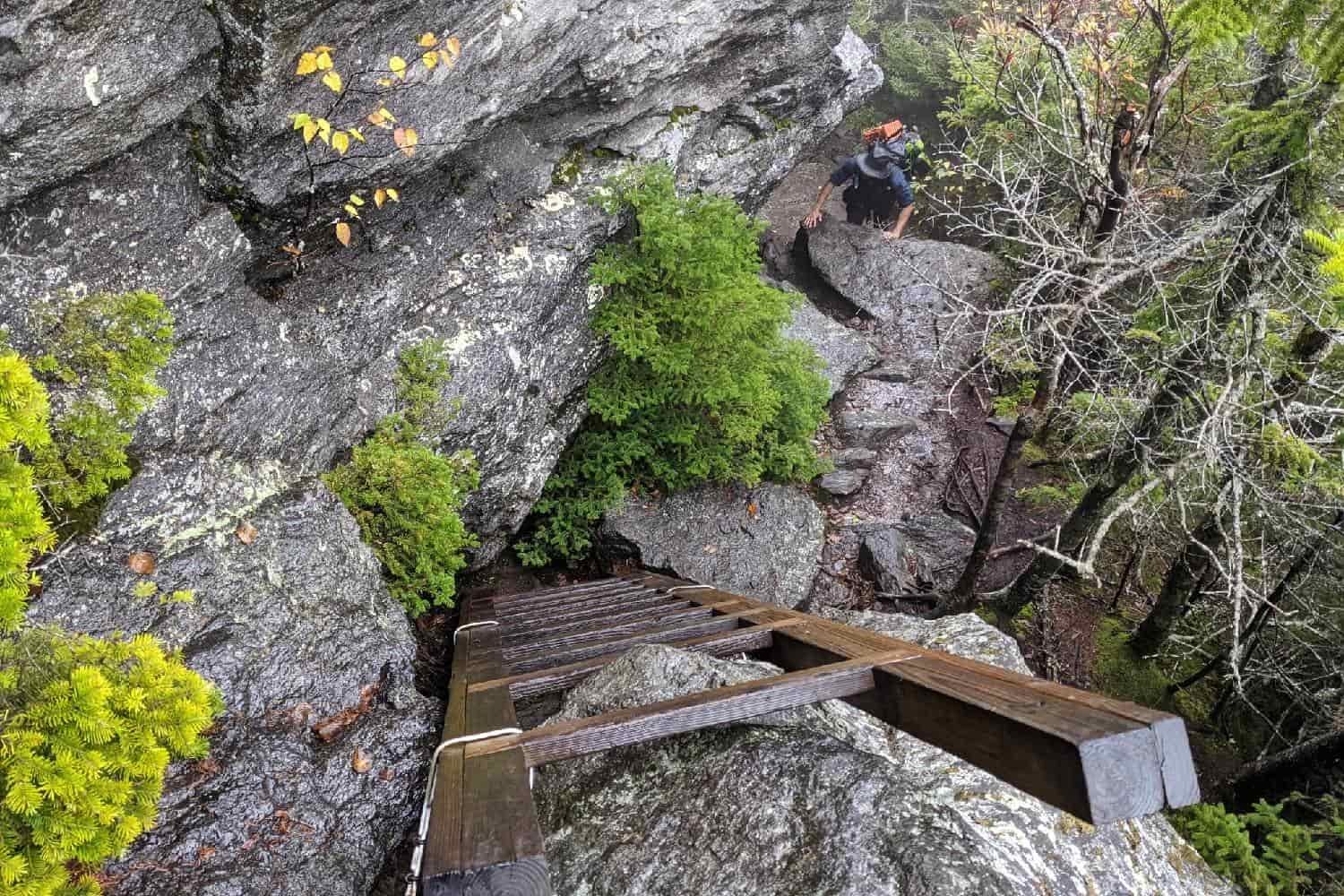 backpacker climbing up rocks to a ladder on the long trail in vermont