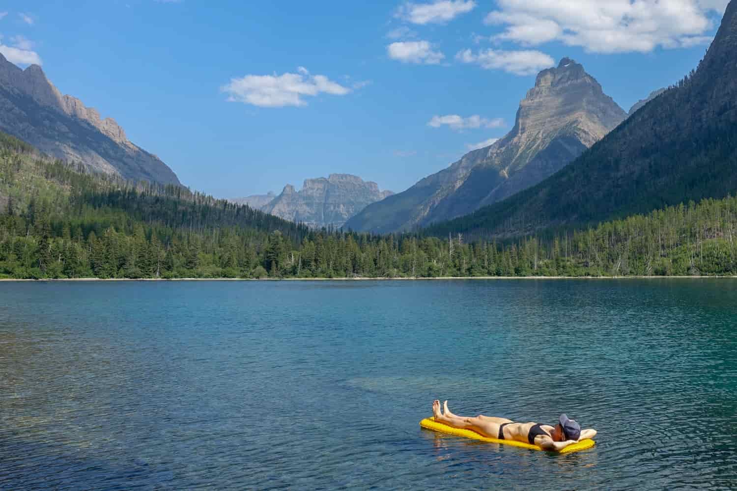 backpacker floating on their sleeping pad on a lake in glacier national park