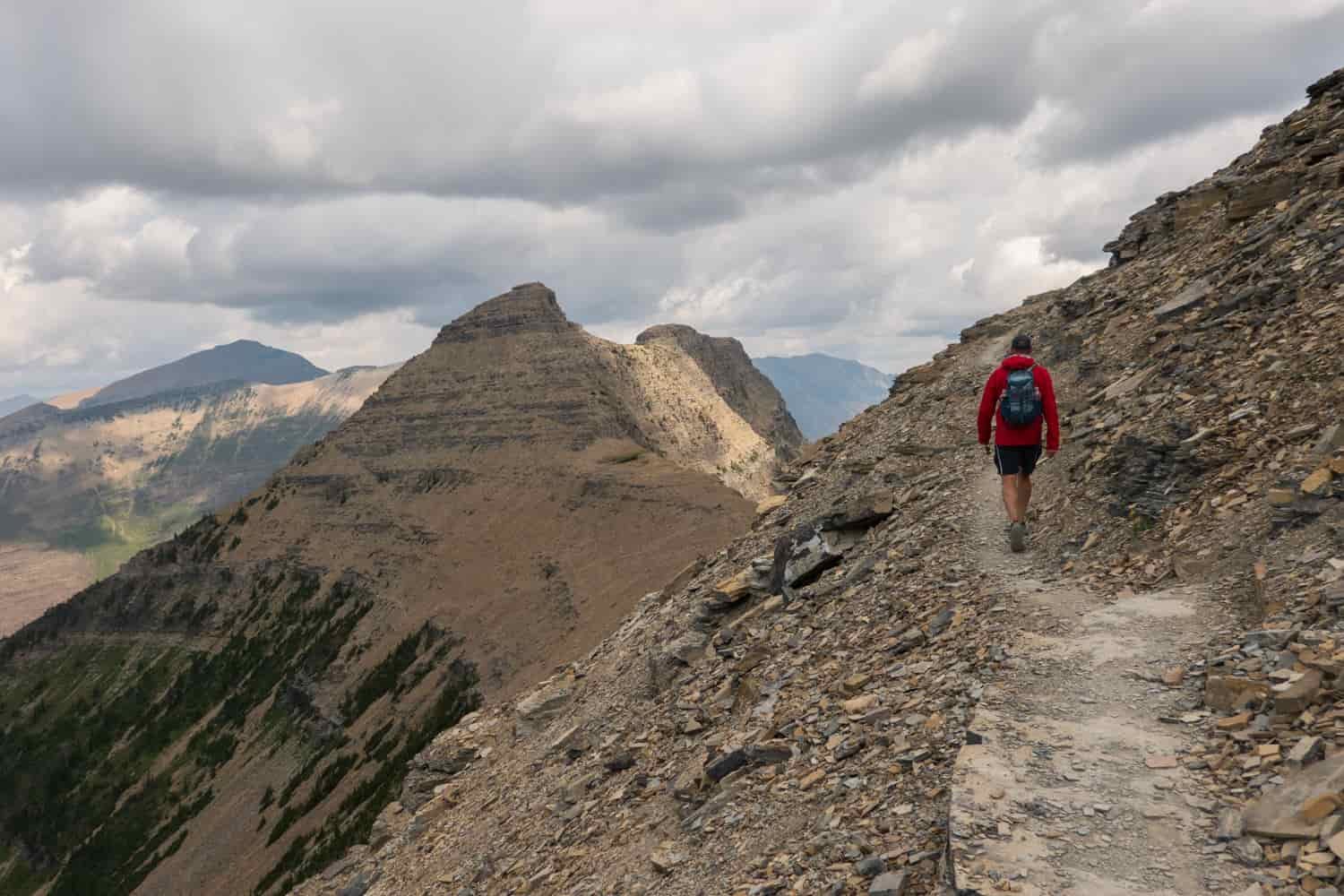 hiker on a rocky trail in glacier national park on a cloudy day