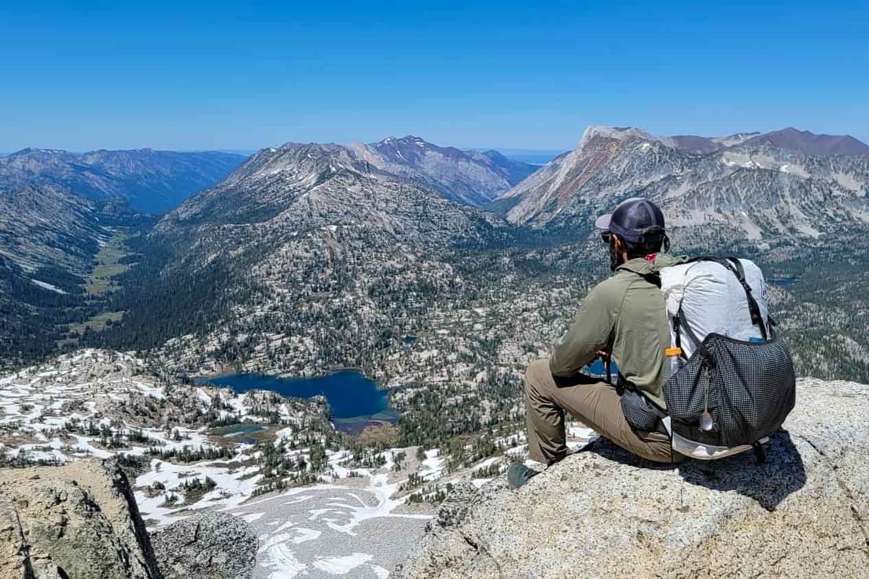backpacker sitting on a large boulder looking out from the summit of eagle cap over lakes and valleys in the wallowa mountains.