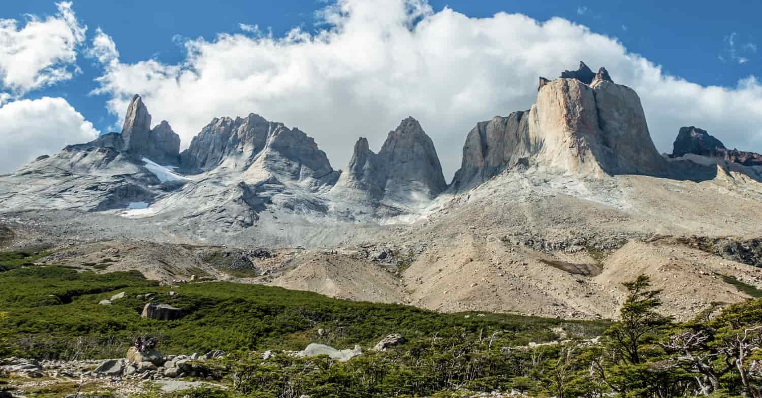 Mountain spires tower over a rocky landscape with white clouds and blue sky above