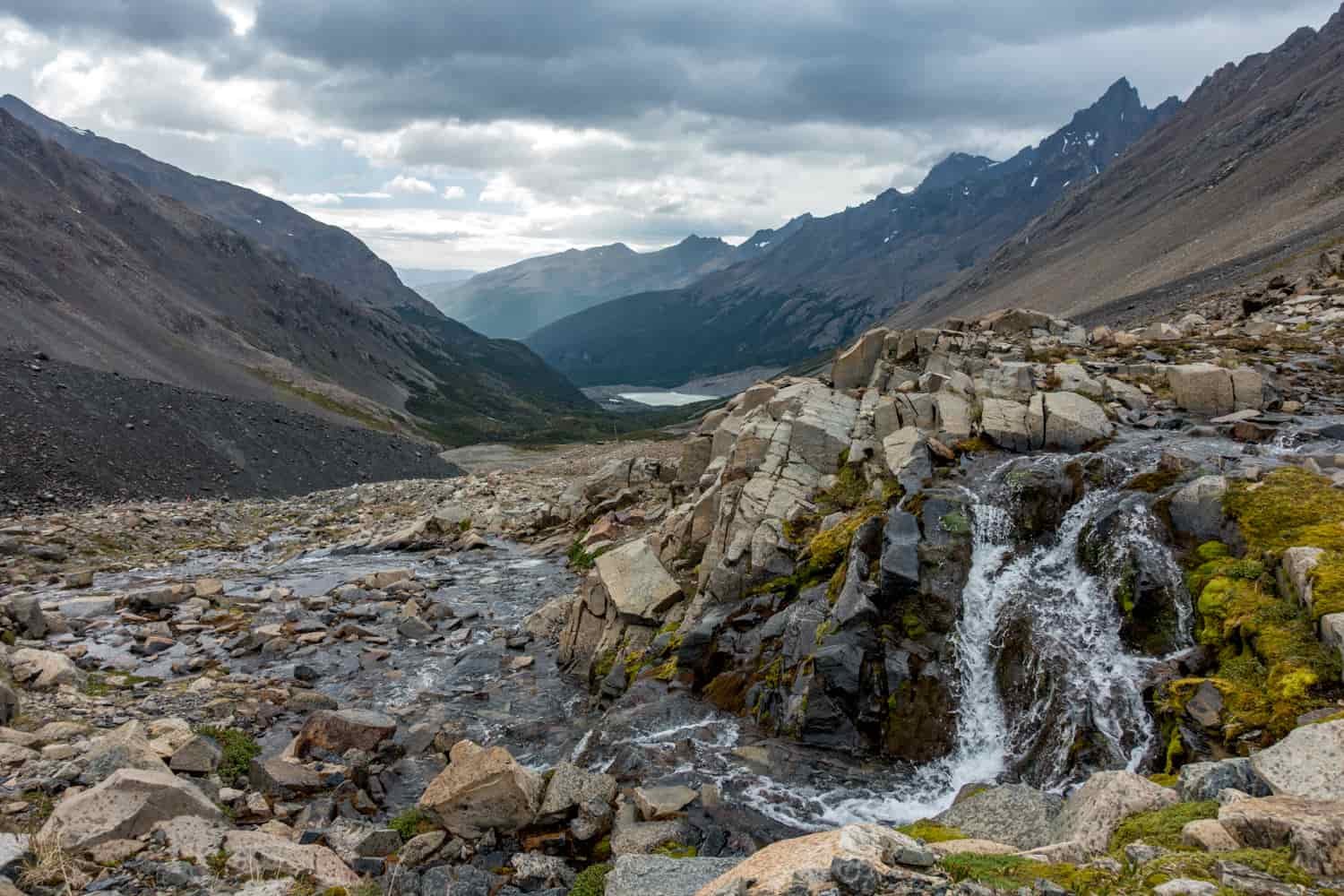 A view looking down a rocky valley with mountains on either side and a rushing brook in the foreground