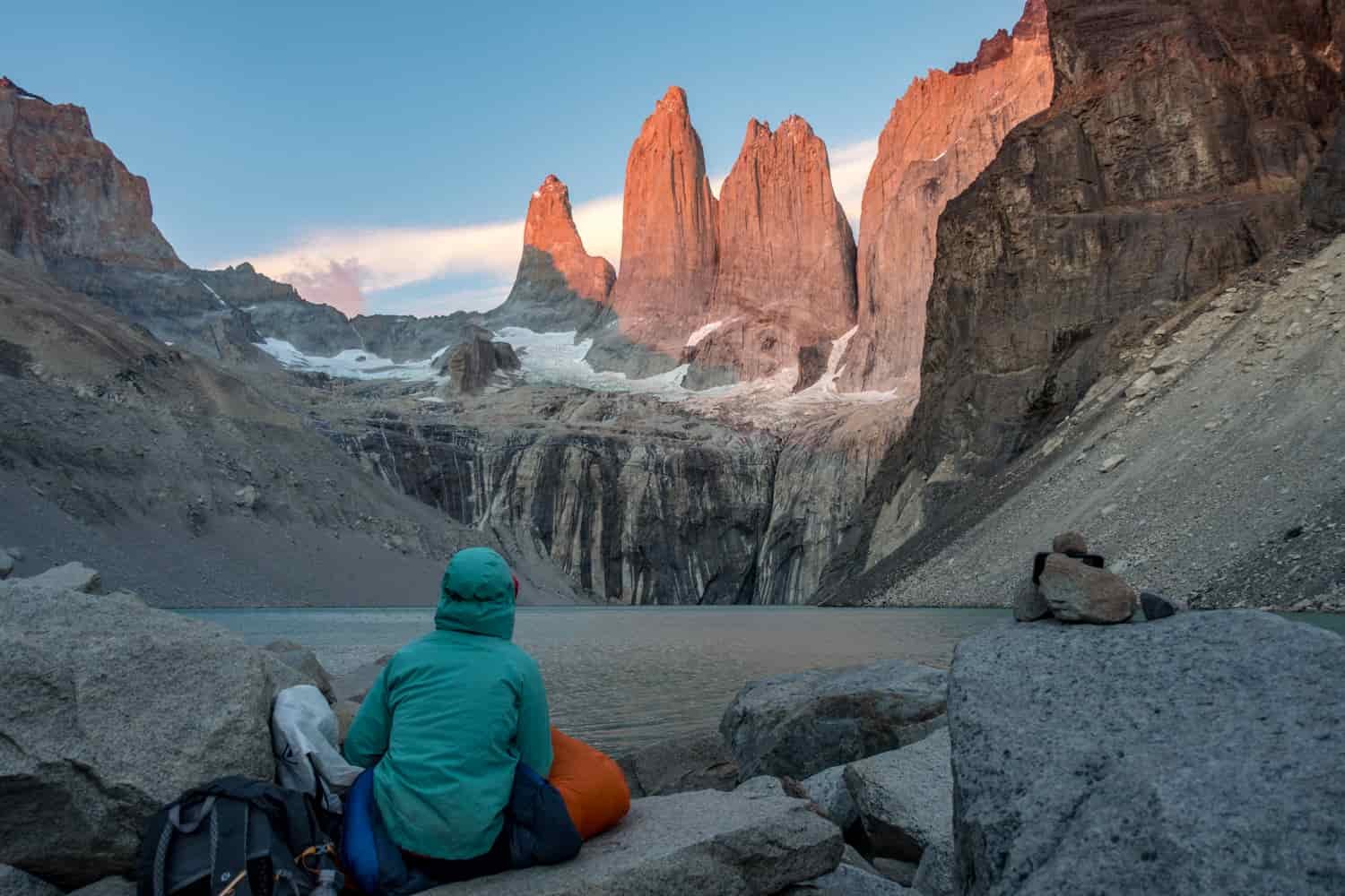 A hiker in a sleeping bag stares at rock spires lit by the sunset