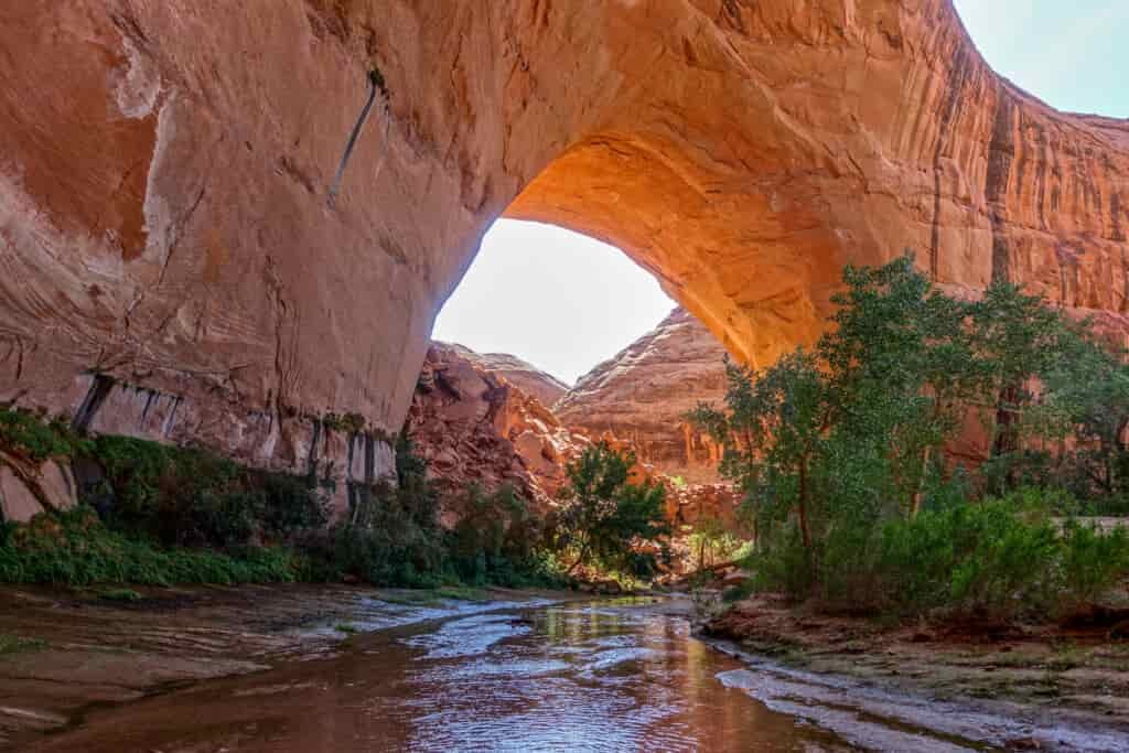 A orange rock arch with a calm river floating under it