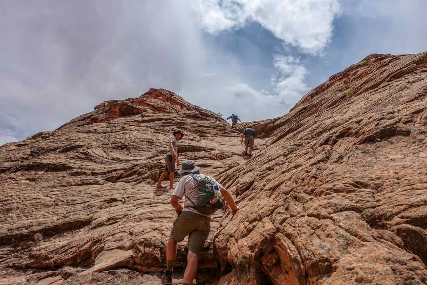 a group of four hikers asends a rock face toward the sky