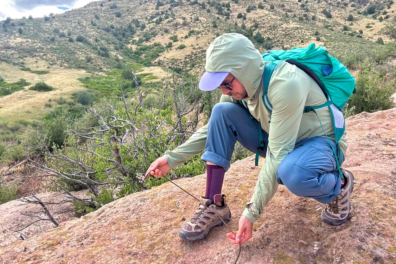 A male hiker ties his shoes in a hunched over position to show off the length of the shoelaces on the Merrell Moab 3s.