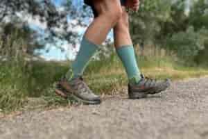 A hiker from the knees down walks on a trail in a forest setting.