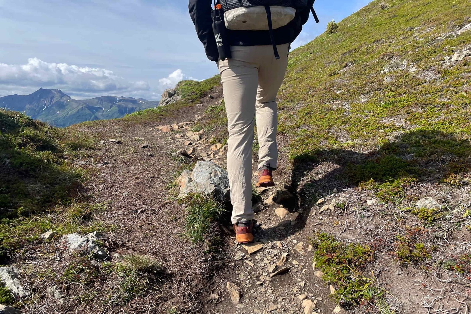 A man walks away from the camera on an alpine trail.