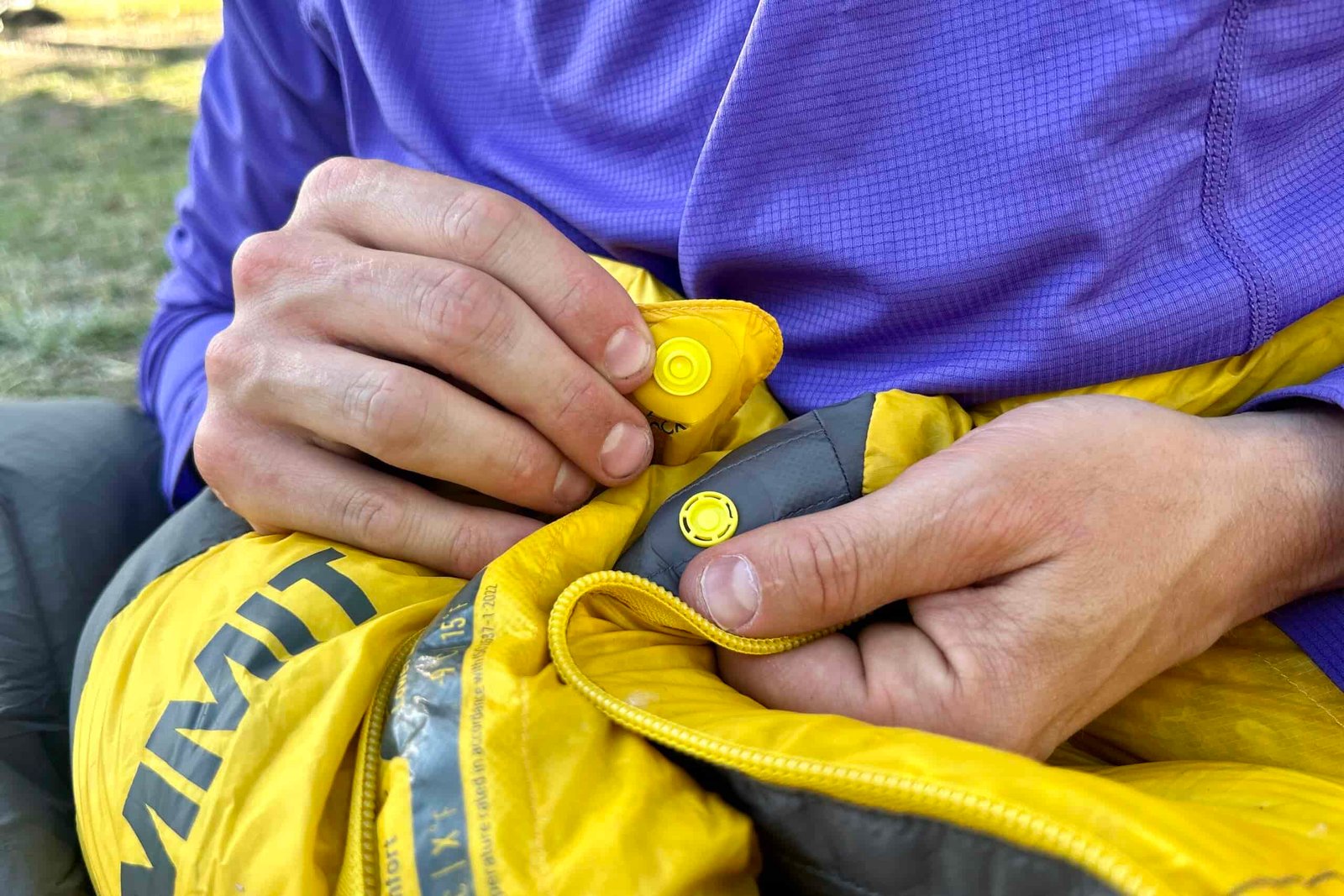 A close-up of a man snapping together two buttons at the top of a sleeping bag.