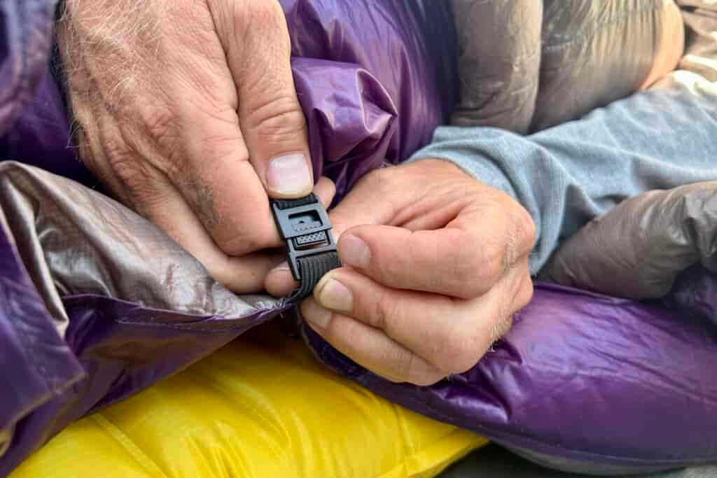 A person clips together the under-mattress attachment points of their quilt.