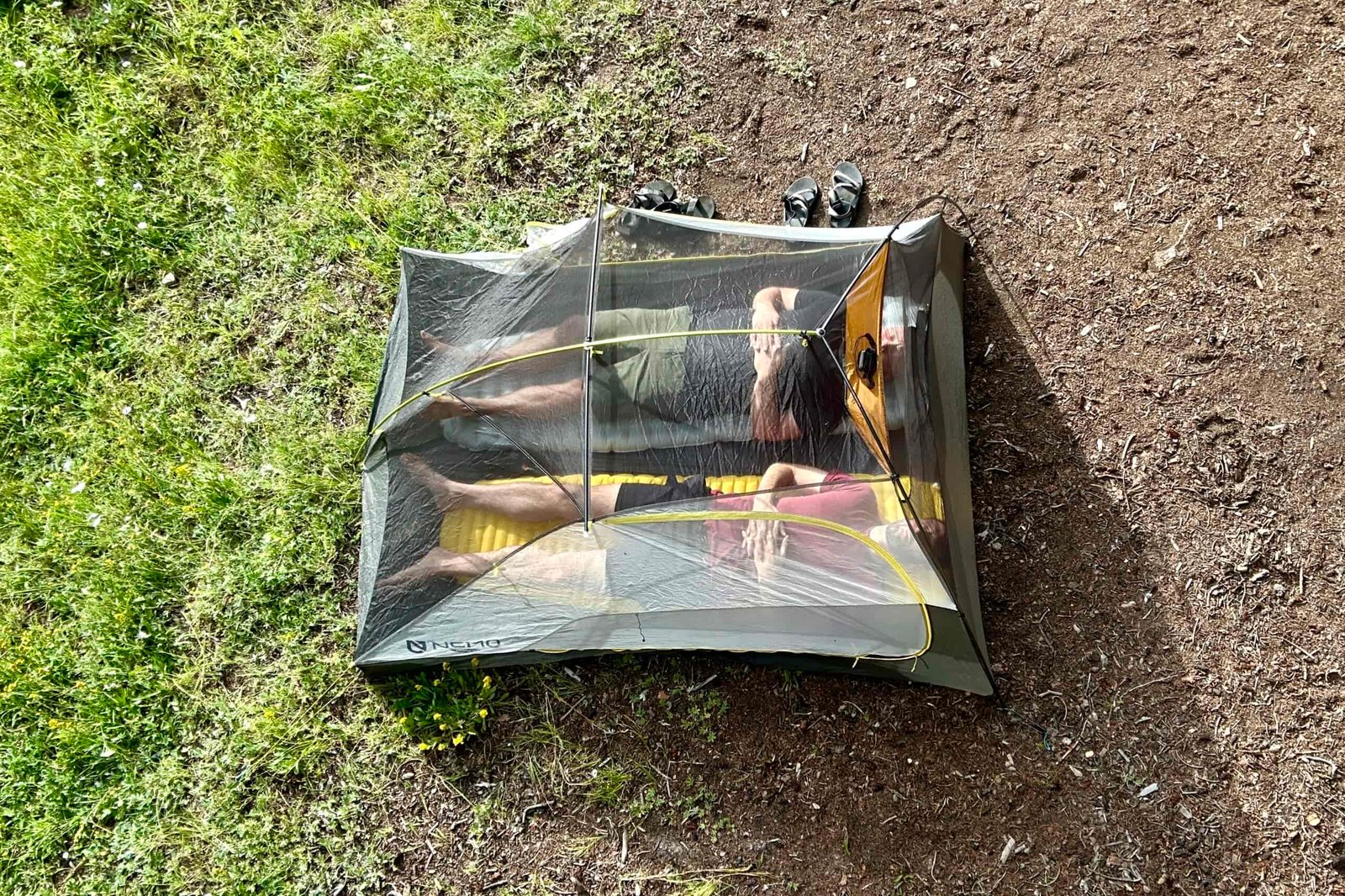 A shot from above of a tent with two men inside, laying on sleeping pads next to each other.