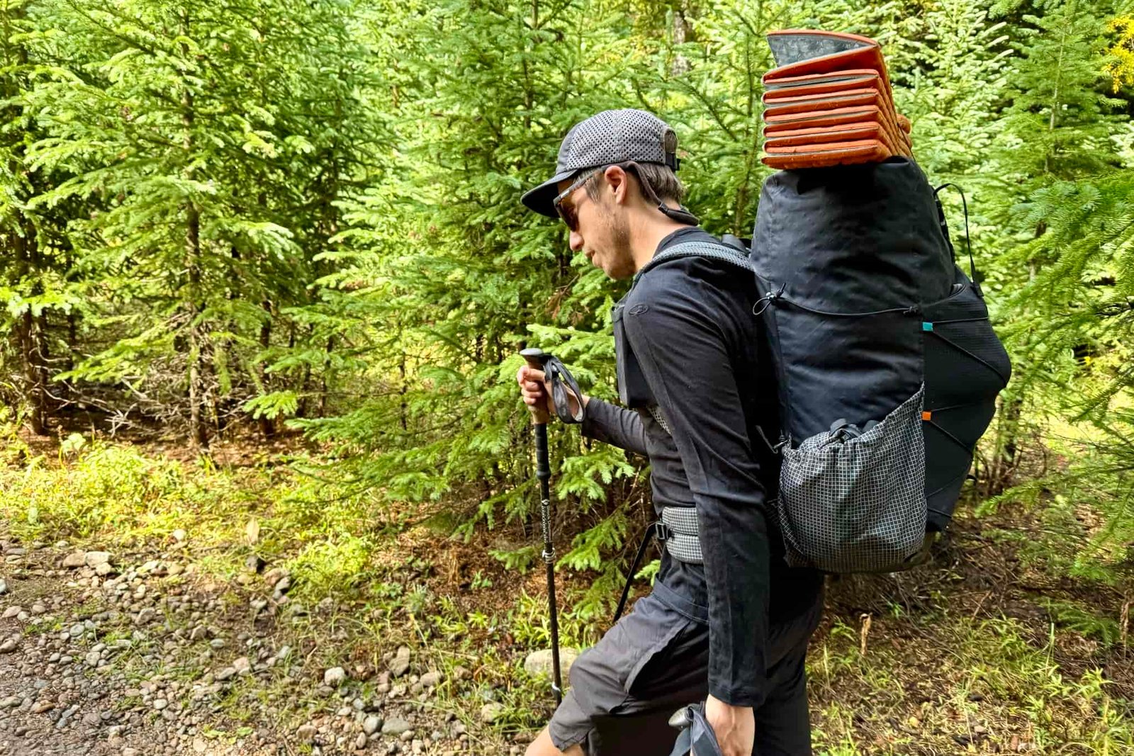 A hiker walks through the woods with a pack while wearing the Icebreaker Oasis 200 base layer. Trees are in the background.