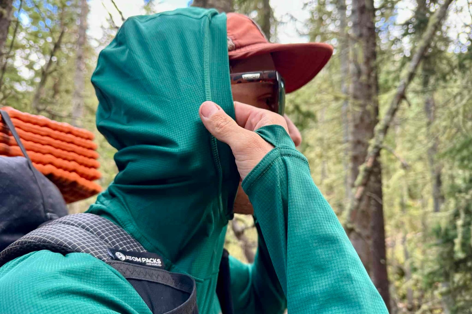 A hiker pulls up the hood on his Outdoor Research Echo Hoodie. Trees are in the background.
