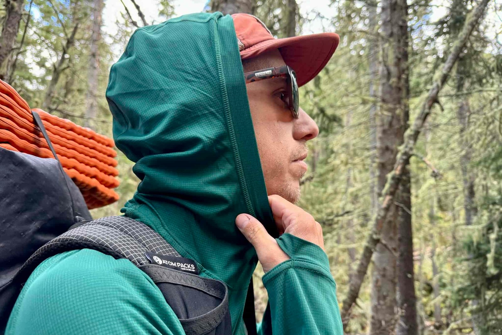 A hiker pulls up the hood on his Outdoor Research Echo Hoodie. Trees are in the background.