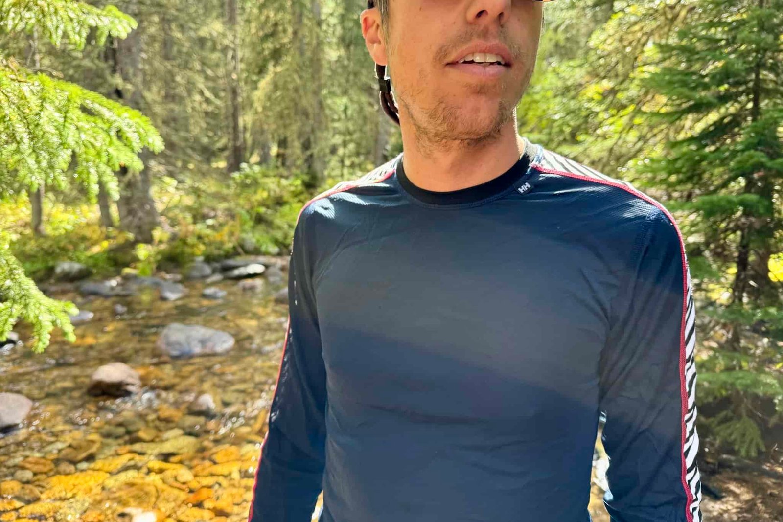 A closeup of a hiker's torso while wearing the Helly Hansen Lifa Stripe base layer. Trees and a creek are in the background.