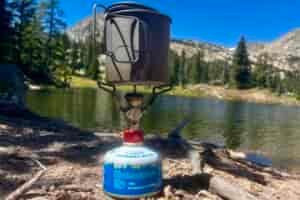 The PocketRocket 2 installed on a fuel canister and holding a pot with mountains and a lake in the background.