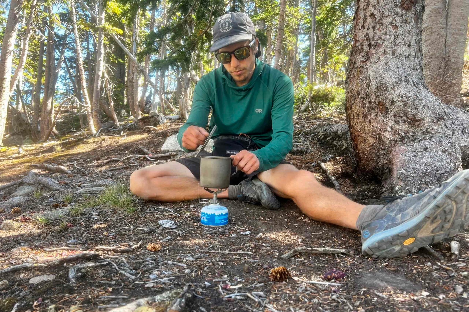 A hiker lifts the lid of his pot while cooking with the BRS 3000T in a wooded setting.