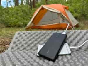 The Anker and a phone sit in front of a tent in the woods.