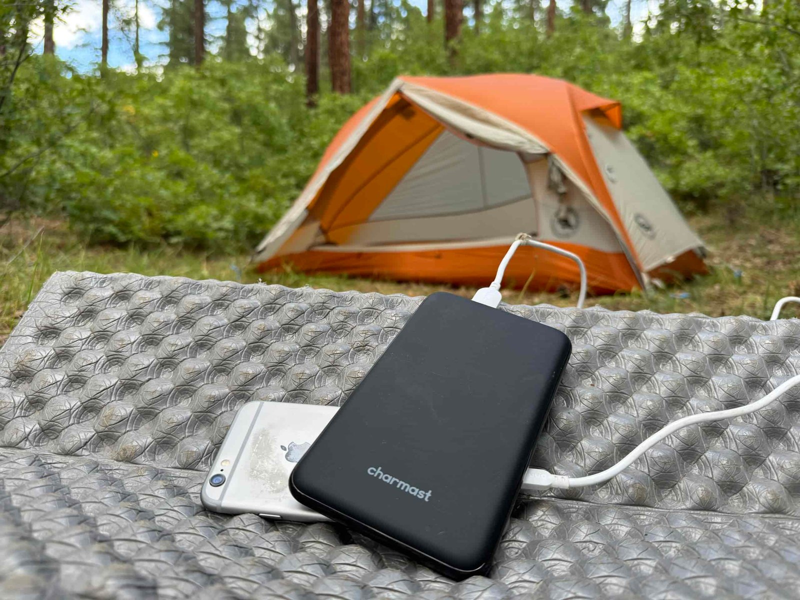 The Charmast and a phone sit in front of a tent in the woods.