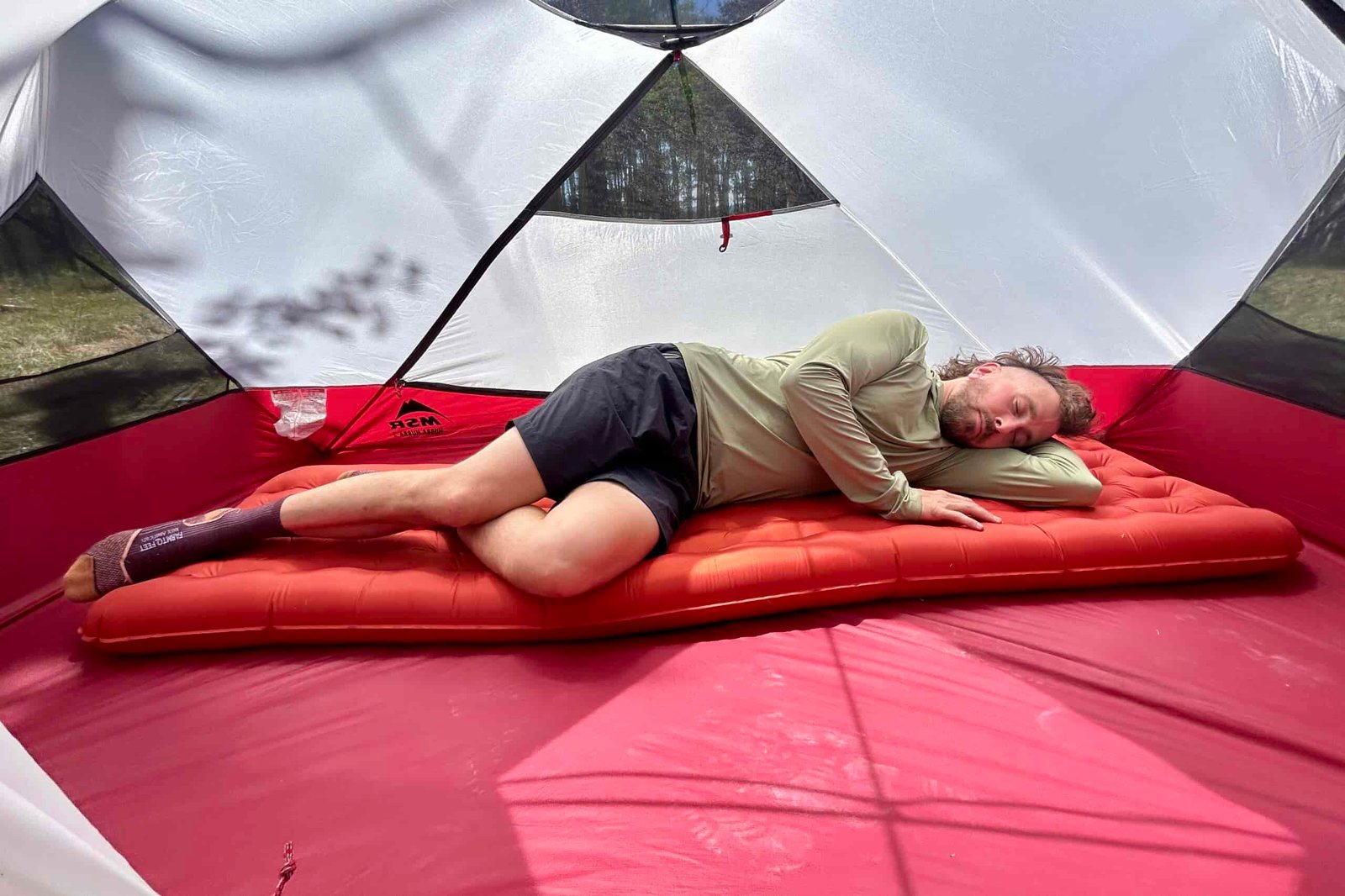 A person sleeps on their side on a red inflatable sleeping pad inside a tent.