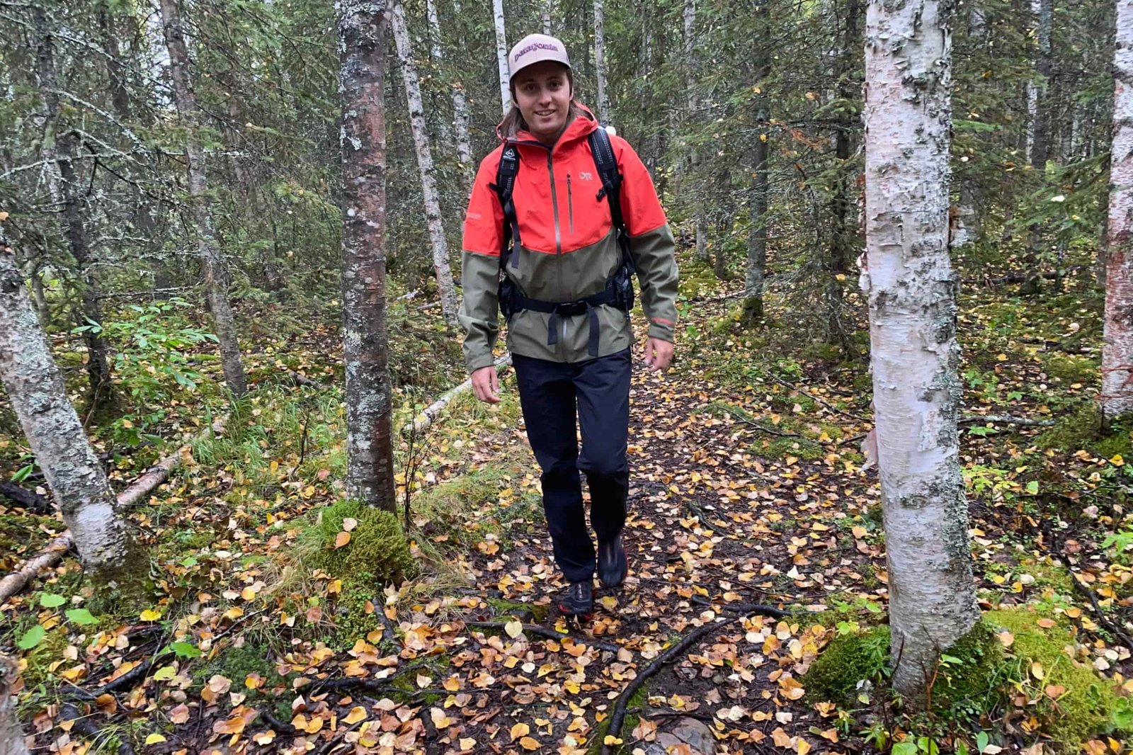 A man walks through a forest with yellow leaves on the ground.