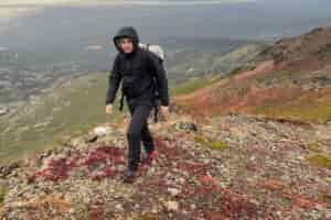 A man hikes uphill with a coastal view behind him.