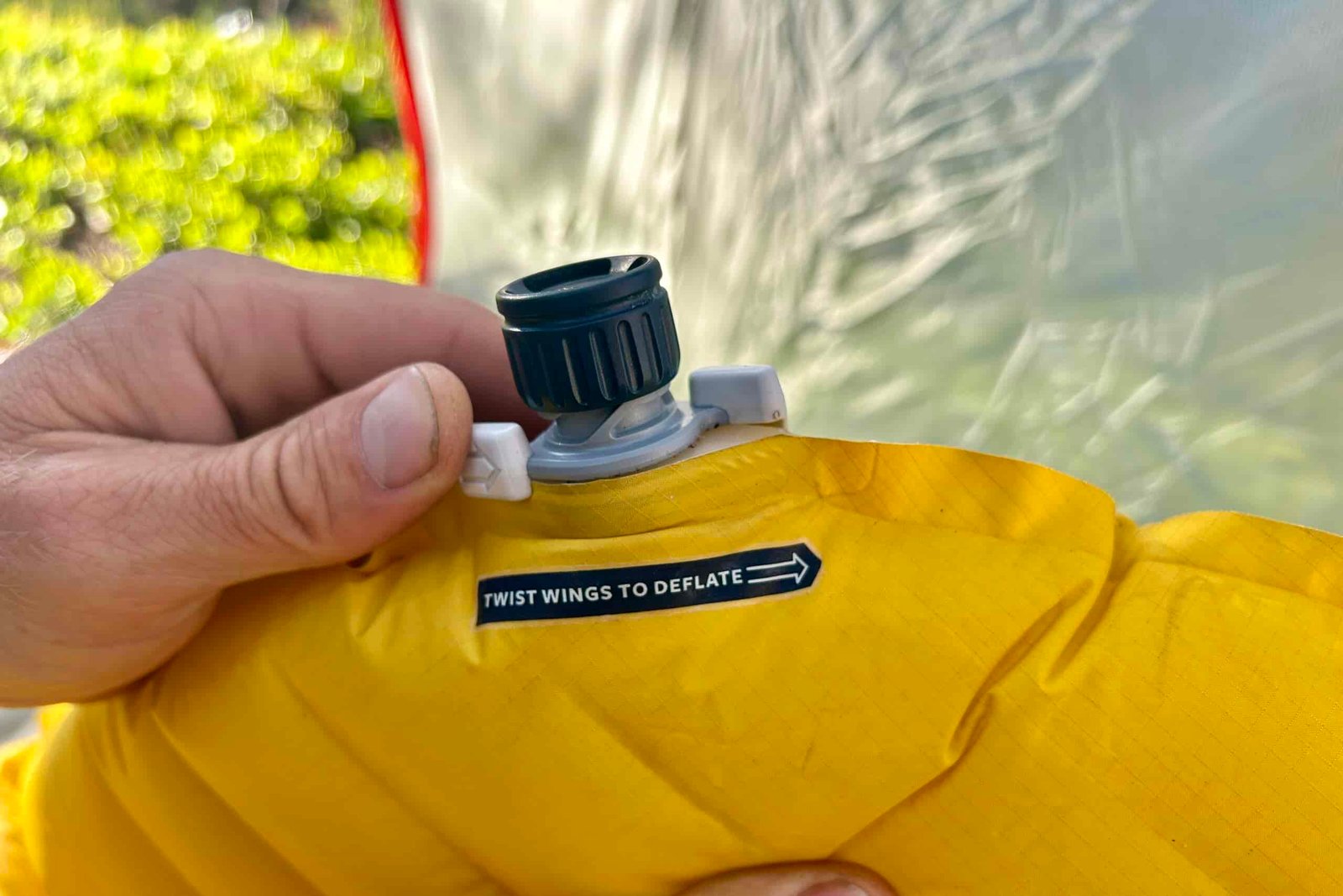 A pair of hands opens the valve of a sleeping pad.