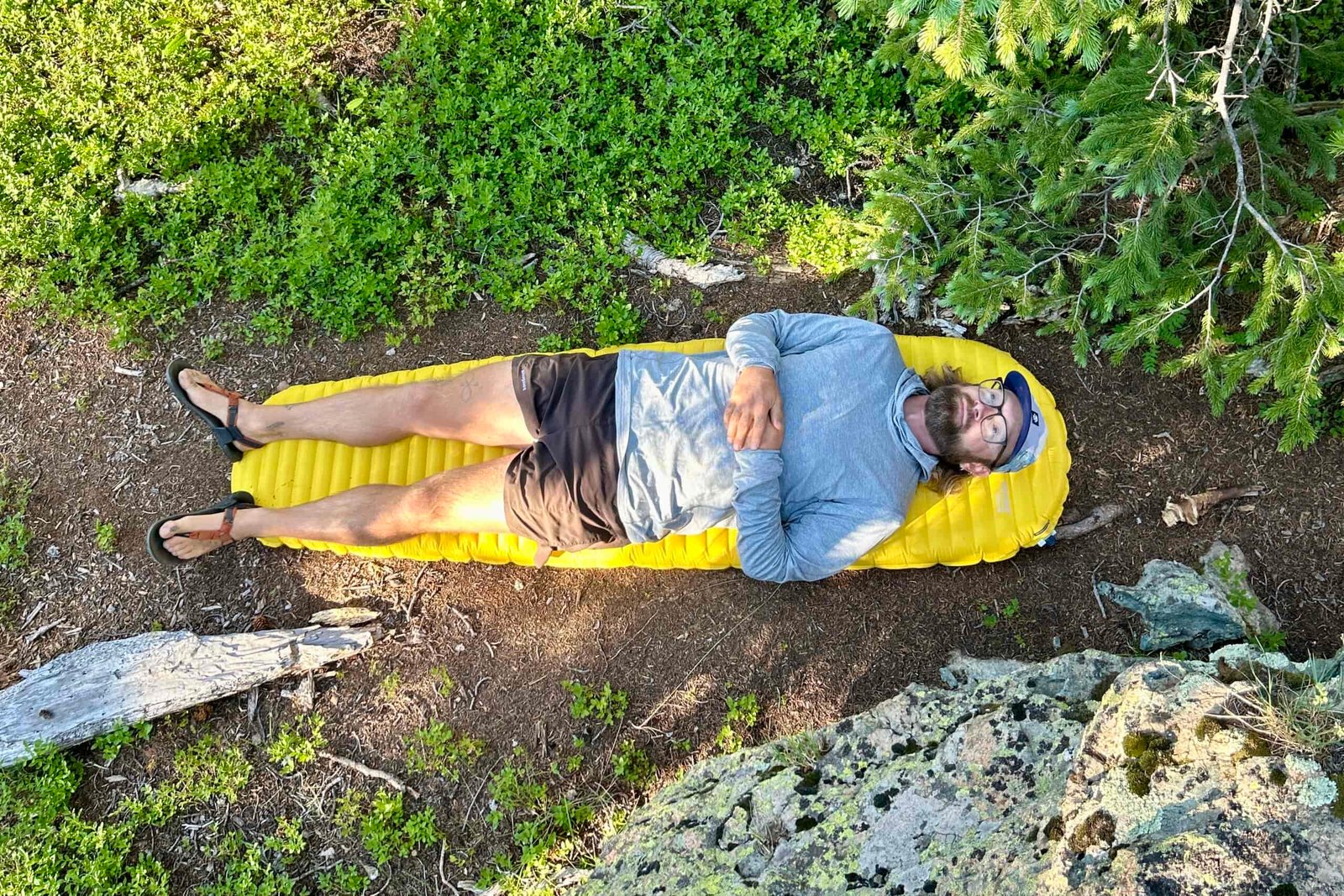 A man is lying on an inflatable mattress on the dirt on a sunny day.