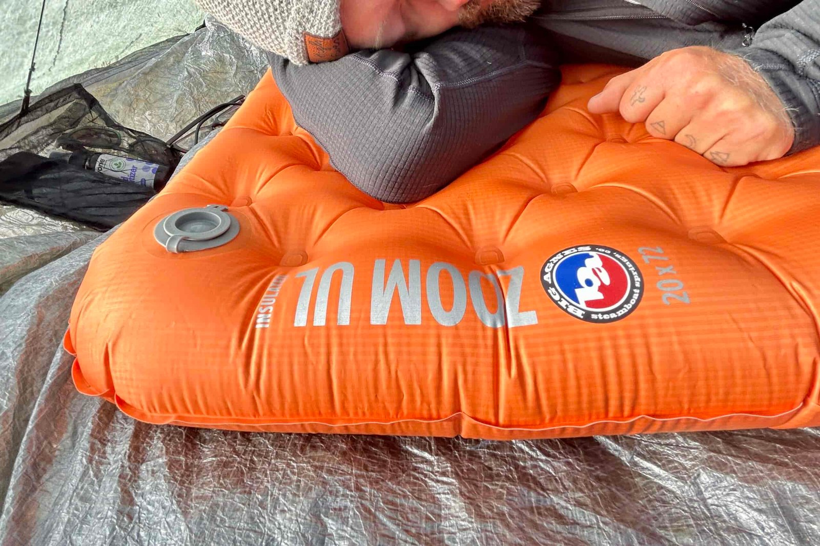 Close up of a man relaxing on an orange sleeping pad in a tent