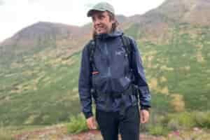 A man smiles while wearing a rain jacket in the alpine.