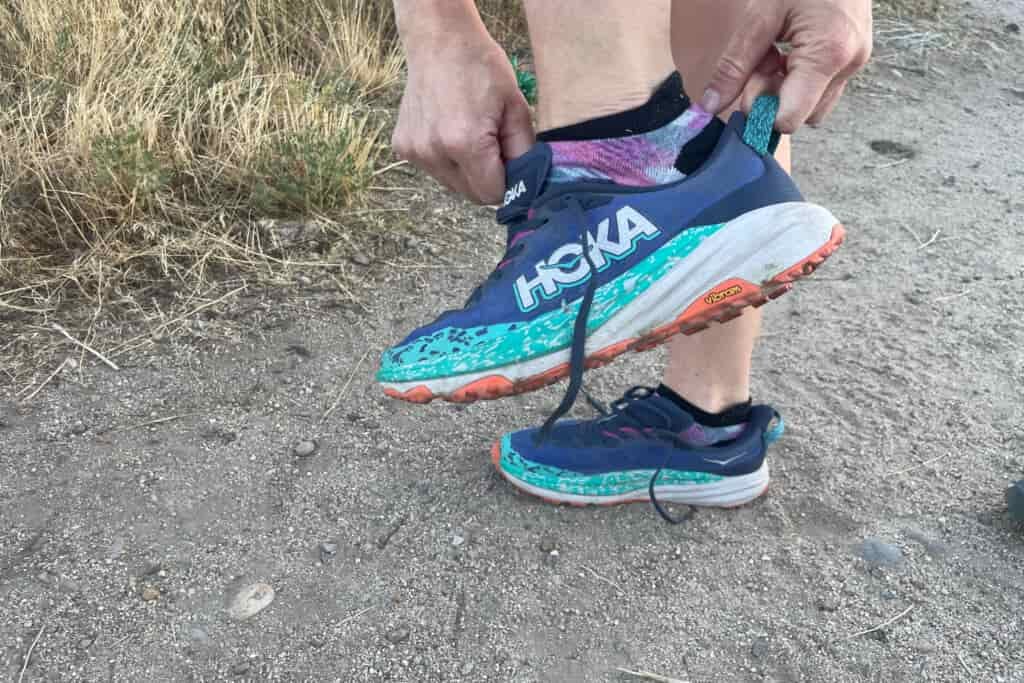 a hiker pulling on the hoka speedgoat 6 onto their foot with the tongue and heel loop