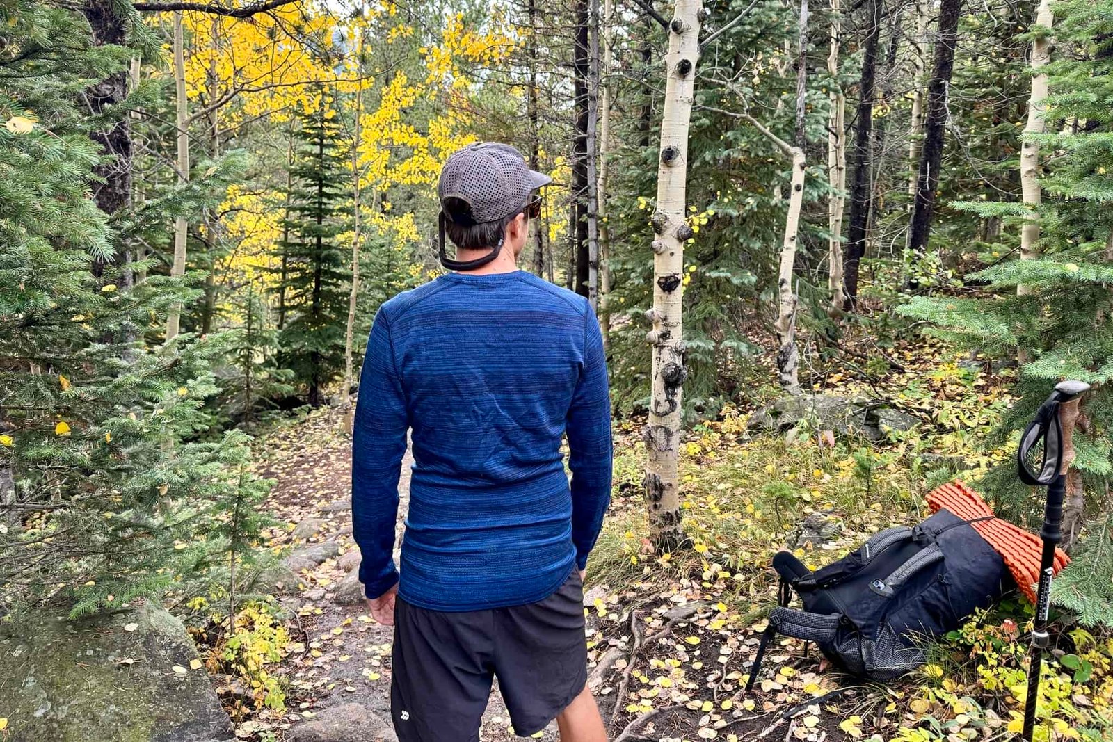 A hiker faces away from the camera wearing the Smartwool Classic Thermal base layer. A pack and trees are in the background.