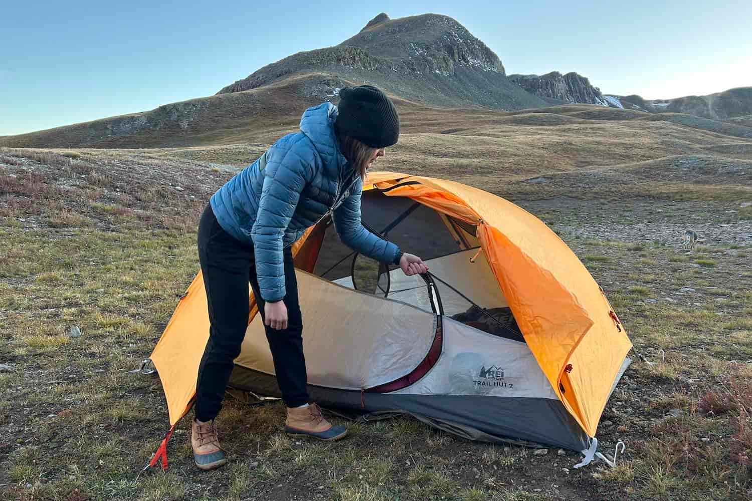 A woman zips closed the door of a tent in the mountains.