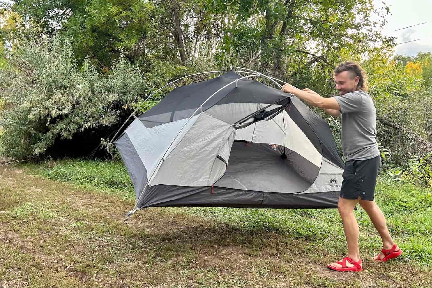 A smiling man lifts and moves a tent.