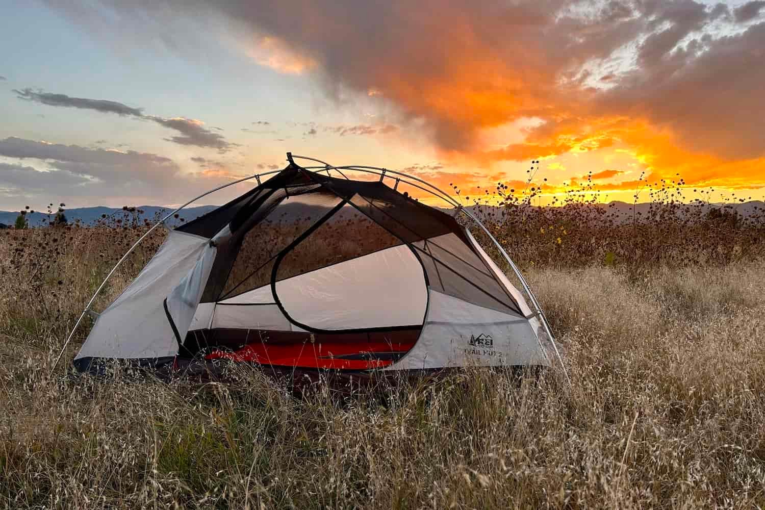 A tent with no fly on sits in a grassy field with a sunset in the background.